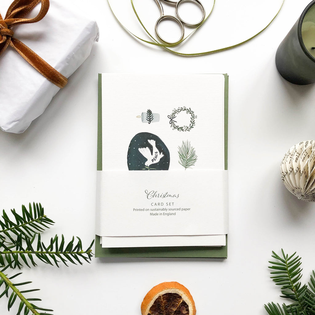 peace dove hand illustrated christmas card set with green envelopes packed on table with pine branches & christmas wrap