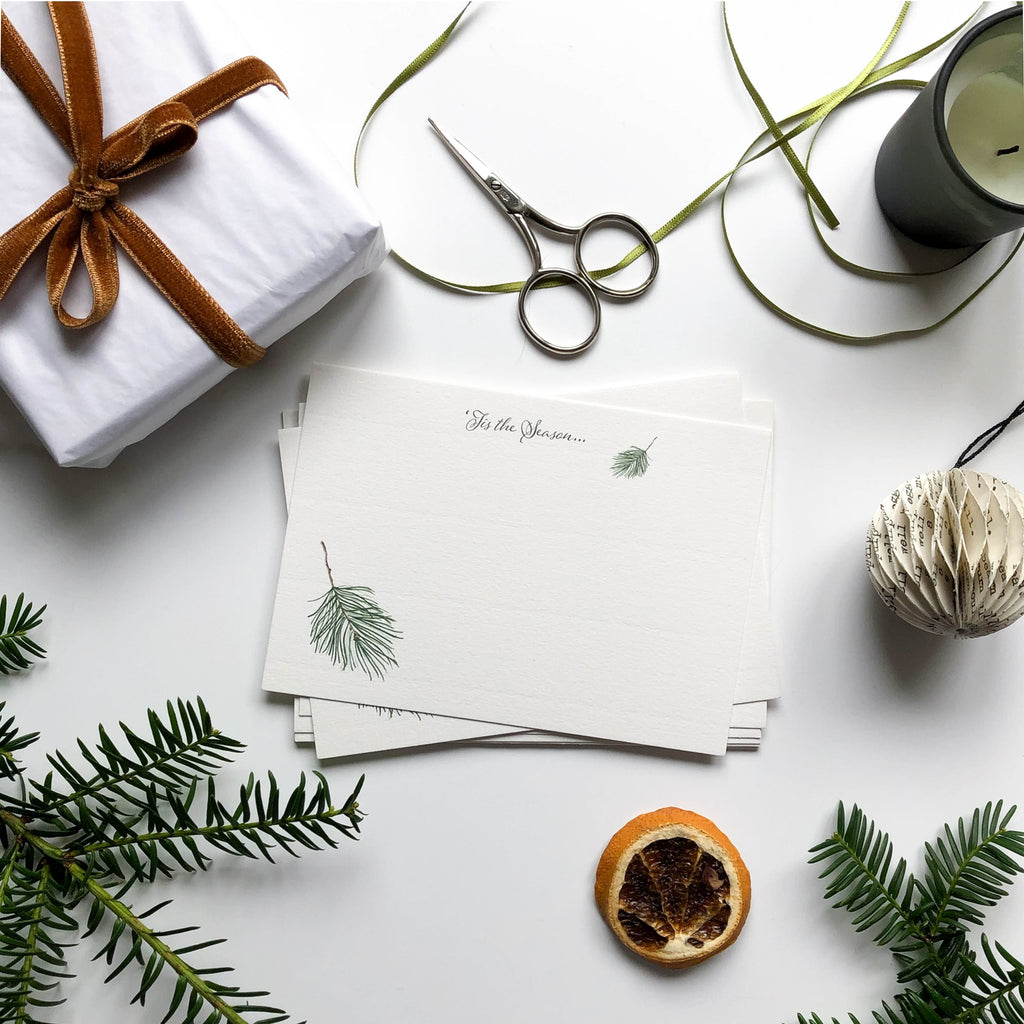 tis the season flat notecard set on table with gift wrap, pine branches & orange slice