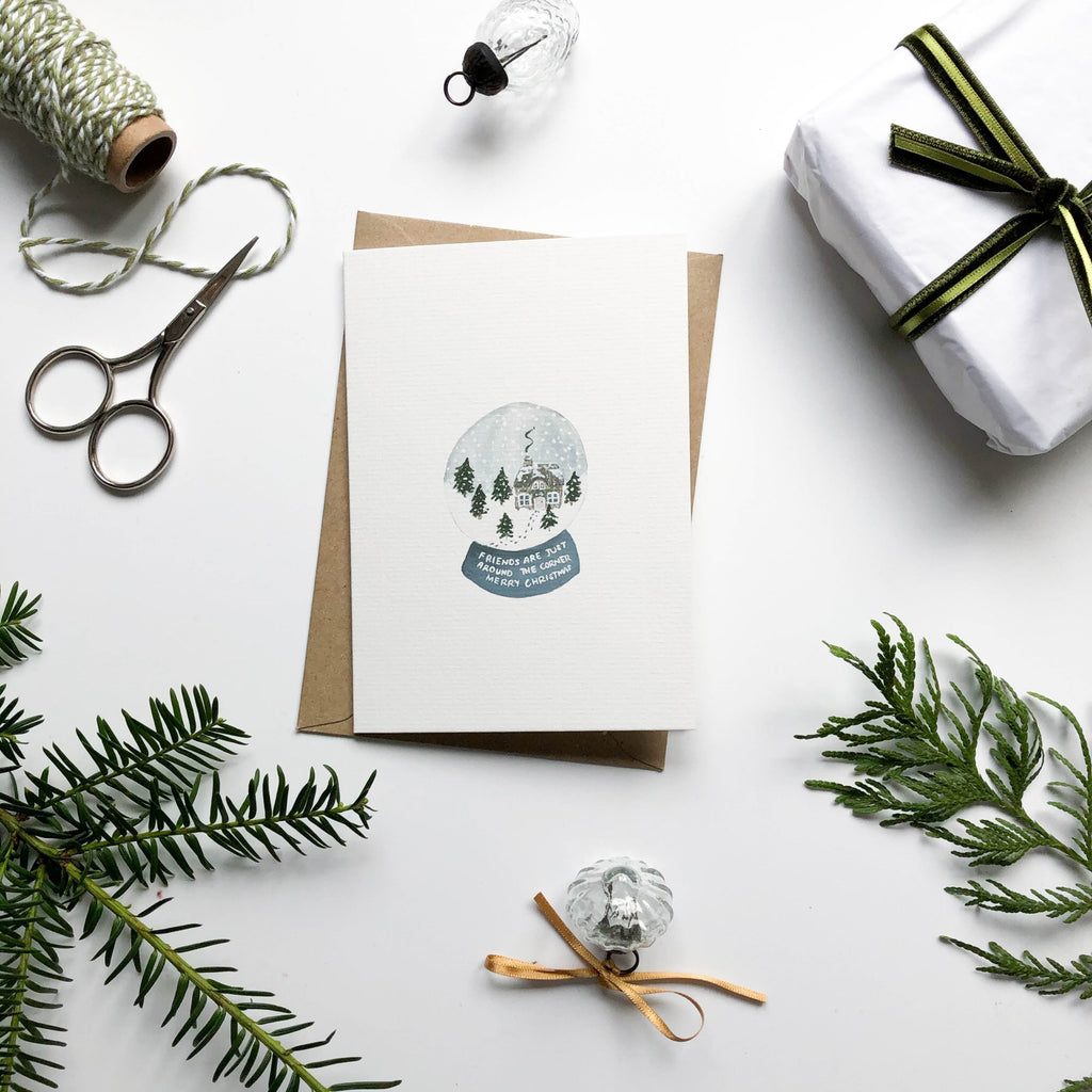 snow globe hand illustrated christmas card in christmas scene with gift wrap & pine branches 