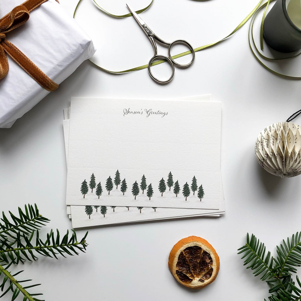 christmas flat notecard set with hand illustrated pine forest on table with orange slice, gift wrap & pine branches